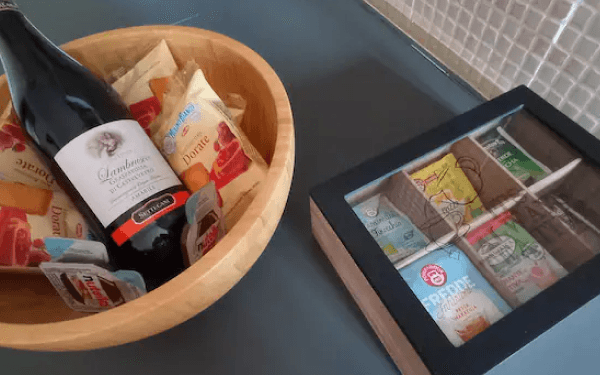 Cesto di benvenuto con bottiglia di Lambrusco, snack e scatola di tisane sul piano cucina