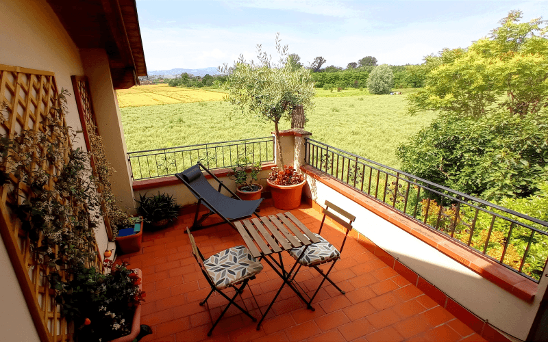 Terrazzo in cotto con tavolo, sedie e sdraio affacciato sui campi coltivati e sulle colline modenesi in estate
